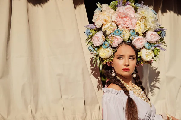 Brunett flicka i en vit ukrainsk autentisk nationell kostym och en krans av blommor poserar mot en terrass. Närbild. — Stockfoto