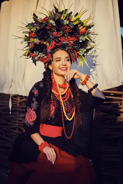 Brunett flicka i en vit ukrainsk autentisk nationell kostym och en krans av blommor poserar mot en terrass. Närbild. — Stockfoto