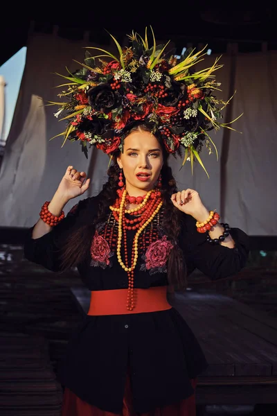 Chica morena en un traje nacional auténtico ucraniano blanco y una corona de flores está posando contra una terraza. Primer plano . — Foto de Stock