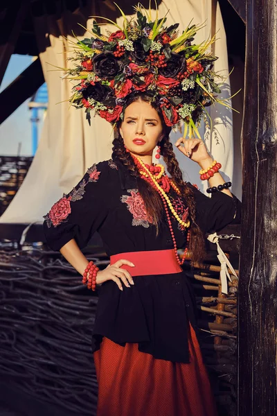 Bruna ragazza in un bianco ucraino autentico costume nazionale e una corona di fiori è in posa contro una terrazza. Primo piano . — Foto Stock