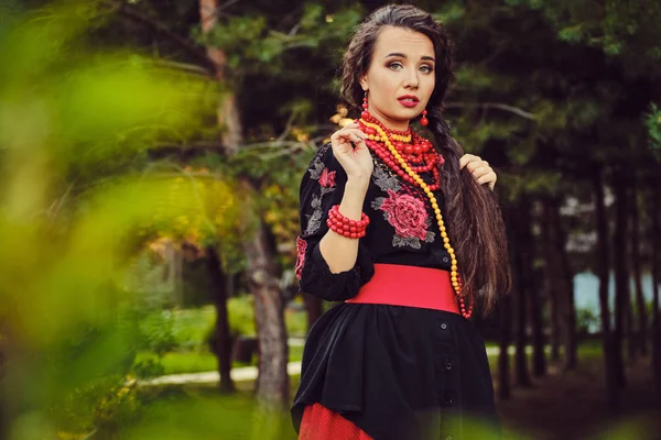 Chica morena en un traje nacional auténtico ucraniano blanco y una corona de flores está posando en un bosque. Primer plano . —  Fotos de Stock