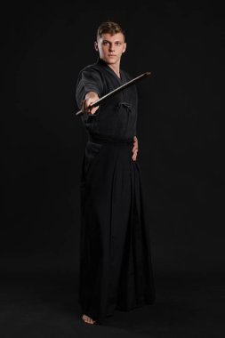 Geleneksel Japon kimonosu giymiş Kendo gurusu Shinai bambu kılıcıyla siyah bir stüdyoda dövüş sanatları eğitimi alıyor..