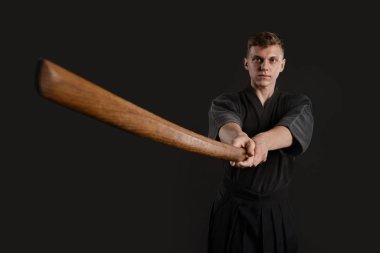 Geleneksel Japon kimonosu giymiş Kendo gurusu Shinai bambu kılıcıyla siyah bir stüdyoda dövüş sanatları eğitimi alıyor..