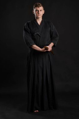 Geleneksel Japon kimonosu giymiş Kendo gurusu Shinai bambu kılıcıyla siyah bir stüdyoda dövüş sanatları eğitimi alıyor..