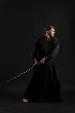 Geleneksel Japon kimonosu giymiş Kendo gurusu Shinai bambu kılıcıyla siyah bir stüdyoda dövüş sanatları eğitimi alıyor..