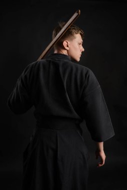 Geleneksel Japon kimonosu giymiş Kendo gurusu Shinai bambu kılıcıyla siyah bir stüdyoda dövüş sanatları eğitimi alıyor..