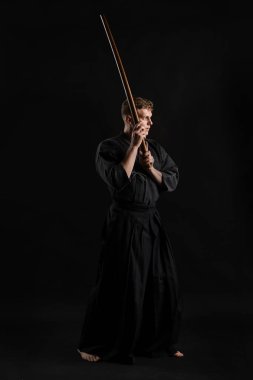 Geleneksel Japon kimonosu giymiş Kendo gurusu Shinai bambu kılıcıyla siyah bir stüdyoda dövüş sanatları eğitimi alıyor..