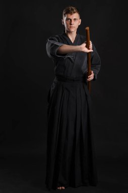 Geleneksel Japon kimonosu giymiş Kendo gurusu Shinai bambu kılıcıyla siyah bir stüdyoda dövüş sanatları eğitimi alıyor..