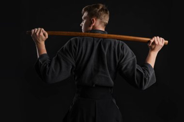 Geleneksel Japon kimonosu giymiş Kendo gurusu Shinai bambu kılıcıyla siyah bir stüdyoda dövüş sanatları eğitimi alıyor..