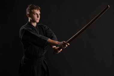 Geleneksel Japon kimonosu giymiş Kendo gurusu Shinai bambu kılıcıyla siyah bir stüdyoda dövüş sanatları eğitimi alıyor..
