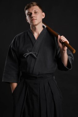 Geleneksel Japon kimonosu giymiş Kendo gurusu Shinai bambu kılıcıyla siyah bir stüdyoda dövüş sanatları eğitimi alıyor..