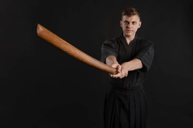 Geleneksel Japon kimonosu giymiş Kendo gurusu Shinai bambu kılıcıyla siyah bir stüdyoda dövüş sanatları eğitimi alıyor..