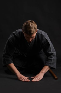 Geleneksel Japon kimonosu giymiş Kendo gurusu Shinai bambu kılıcıyla siyah bir stüdyoda dövüş sanatları eğitimi alıyor..