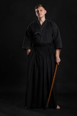 Geleneksel Japon kimonosu giymiş Kendo gurusu Shinai bambu kılıcıyla siyah bir stüdyoda dövüş sanatları eğitimi alıyor..
