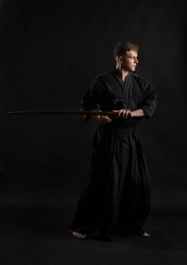 Geleneksel Japon kimonosu giymiş Kendo gurusu Shinai bambu kılıcıyla siyah bir stüdyoda dövüş sanatları eğitimi alıyor..