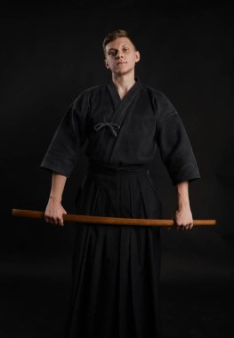 Geleneksel Japon kimonosu giymiş Kendo gurusu Shinai bambu kılıcıyla siyah bir stüdyoda dövüş sanatları eğitimi alıyor..