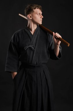 Geleneksel Japon kimonosu giymiş Kendo gurusu Shinai bambu kılıcıyla siyah bir stüdyoda dövüş sanatları eğitimi alıyor..