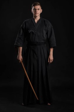 Geleneksel Japon kimonosu giymiş Kendo gurusu Shinai bambu kılıcıyla siyah bir stüdyoda dövüş sanatları eğitimi alıyor..