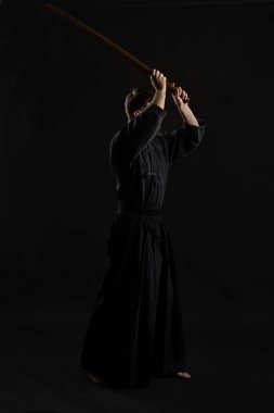 Geleneksel Japon kimonosu giymiş Kendo gurusu Shinai bambu kılıcıyla siyah bir stüdyoda dövüş sanatları eğitimi alıyor..