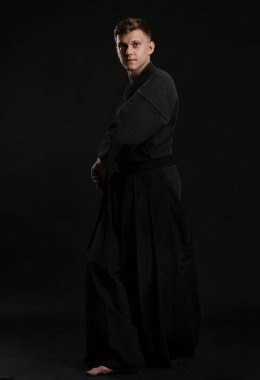 Geleneksel Japon kimonosu giymiş Kendo gurusu Shinai bambu kılıcıyla siyah bir stüdyoda dövüş sanatları eğitimi alıyor..