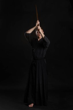 Geleneksel Japon kimonosu giymiş Kendo gurusu Shinai bambu kılıcıyla siyah bir stüdyoda dövüş sanatları eğitimi alıyor..