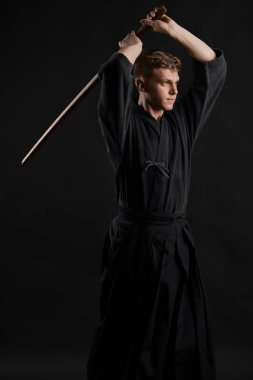 Geleneksel Japon kimonosu giymiş Kendo gurusu Shinai bambu kılıcıyla siyah bir stüdyoda dövüş sanatları eğitimi alıyor..