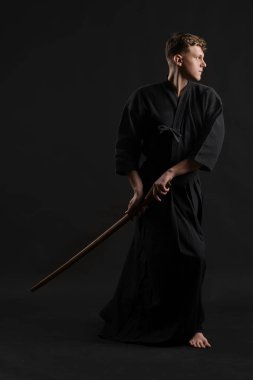 Geleneksel Japon kimonosu giymiş Kendo gurusu Shinai bambu kılıcıyla siyah bir stüdyoda dövüş sanatları eğitimi alıyor..