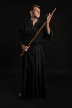 Geleneksel Japon kimonosu giymiş Kendo gurusu Shinai bambu kılıcıyla siyah bir stüdyoda dövüş sanatları eğitimi alıyor..