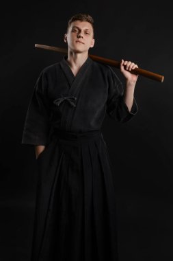 Geleneksel Japon kimonosu giymiş Kendo gurusu Shinai bambu kılıcıyla siyah bir stüdyoda dövüş sanatları eğitimi alıyor..