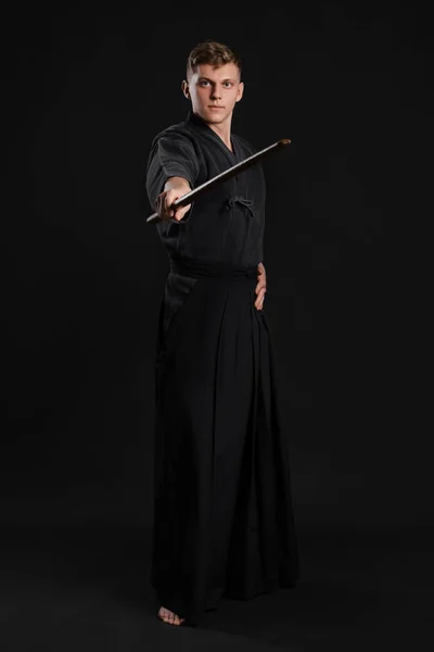 Kendo guru na sobě v tradičním japonském kimonu cvičí bojové umění s bambusovým mečem Shinai na černém pozadí studia. — Stock fotografie