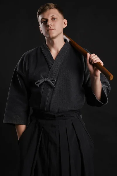 Kendo guru vestindo em um kimono japonês tradicional está praticando arte marcial com a espada de bambu de xadrez contra um fundo de estúdio preto. — Fotografia de Stock