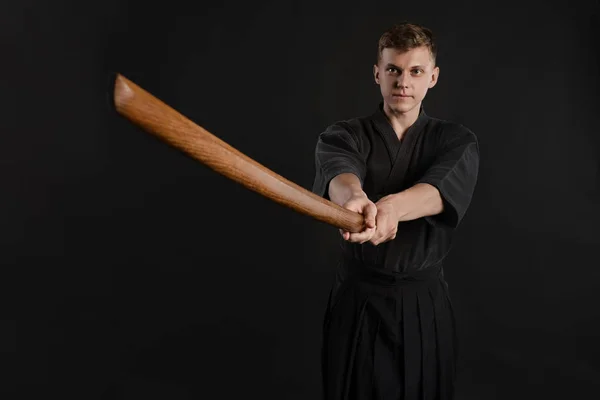 Kendo guru wearing in a traditional japanese kimono is practicing martial art with the shinai bamboo sword against a black studio background. — Stock Photo, Image