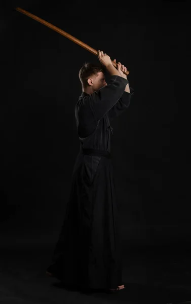 Kendo-Guru im traditionellen japanischen Kimono praktiziert Kampfkunst mit dem Shinai-Bambusschwert vor schwarzem Studiohintergrund. — Stockfoto