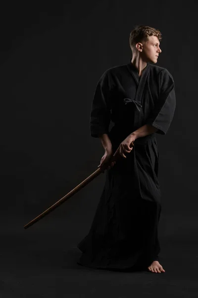 Kendo guru wearing in a traditional japanese kimono is practicing martial art with the shinai bamboo sword against a black studio background. — Stock Photo, Image