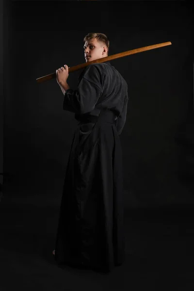 Kendo guru na sobě v tradičním japonském kimonu cvičí bojové umění s bambusovým mečem Shinai na černém pozadí studia. — Stock fotografie