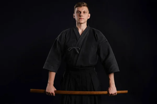 Kendo guru wearing in a traditional japanese kimono is practicing martial art with the shinai bamboo sword against a black studio background. Stock Image