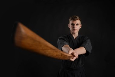 Geleneksel Japon kimonosu giymiş Kendo gurusu Shinai bambu kılıcıyla siyah bir stüdyoda dövüş sanatları eğitimi alıyor..