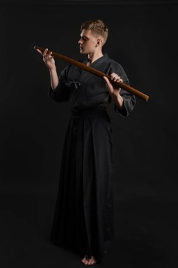 Geleneksel Japon kimonosu giymiş Kendo gurusu Shinai bambu kılıcıyla siyah bir stüdyoda dövüş sanatları eğitimi alıyor..