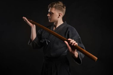 Geleneksel Japon kimonosu giymiş Kendo gurusu Shinai bambu kılıcıyla siyah bir stüdyoda dövüş sanatları eğitimi alıyor..