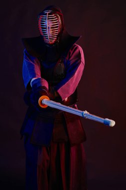 Yakın çekim, Kendo dövüşçüsü zırh giyiyor, geleneksel kimono giyiyor, miğfer takıyor shinai bambu kılıcıyla dövüş sanatları yapıyor, siyah arka plan.
