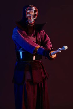 Yakın çekim, Kendo dövüşçüsü zırh giyiyor, geleneksel kimono giyiyor, miğfer takıyor shinai bambu kılıcıyla dövüş sanatları yapıyor, siyah arka plan.