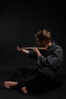 Geleneksel Japon kimonosu giymiş Kendo gurusu Shinai bambu kılıcıyla siyah bir stüdyoda dövüş sanatları eğitimi alıyor..