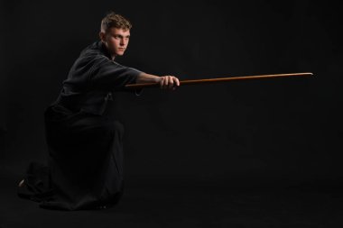 Geleneksel Japon kimonosu giymiş Kendo gurusu Shinai bambu kılıcıyla siyah bir stüdyoda dövüş sanatları eğitimi alıyor..