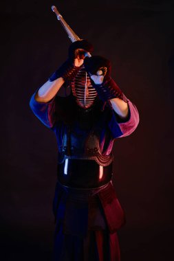 Yakın çekim, Kendo dövüşçüsü zırh giyiyor, geleneksel kimono giyiyor, miğfer takıyor shinai bambu kılıcıyla dövüş sanatları yapıyor, siyah arka plan.
