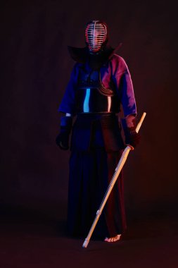 Yakın çekim, Kendo dövüşçüsü zırh giyiyor, geleneksel kimono giyiyor, miğfer takıyor shinai bambu kılıcıyla dövüş sanatları yapıyor, siyah arka plan.