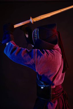 Yakın çekim, Kendo dövüşçüsü zırh giyiyor, geleneksel kimono giyiyor, miğfer takıyor shinai bambu kılıcıyla dövüş sanatları yapıyor, siyah arka plan.