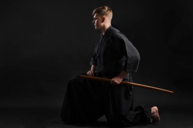 Geleneksel Japon kimonosu giymiş Kendo gurusu Shinai bambu kılıcıyla siyah bir stüdyoda dövüş sanatları eğitimi alıyor..