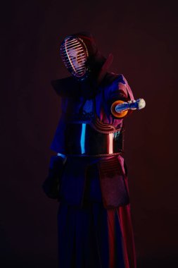 Yakın çekim, Kendo dövüşçüsü zırh giyiyor, geleneksel kimono giyiyor, miğfer takıyor shinai bambu kılıcıyla dövüş sanatları yapıyor, siyah arka plan.