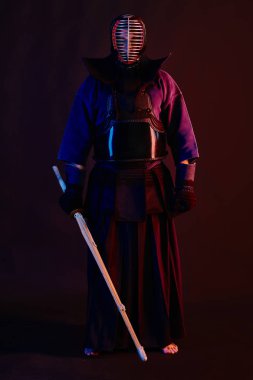 Yakın çekim, Kendo dövüşçüsü zırh giyiyor, geleneksel kimono giyiyor, miğfer takıyor shinai bambu kılıcıyla dövüş sanatları yapıyor, siyah arka plan.