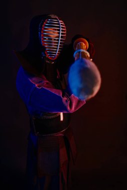 Yakın çekim, Kendo dövüşçüsü zırh giyiyor, geleneksel kimono giyiyor, miğfer takıyor shinai bambu kılıcıyla dövüş sanatları yapıyor, siyah arka plan.